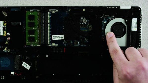 A person's finger touching an unpainted metal surface on the back of a laptop computer turned upside down to discharge static electricity.
