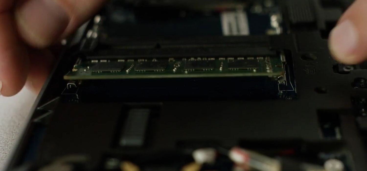 A person undoing the side clips of a Crucial RAM memory module to remove it from a laptop computer